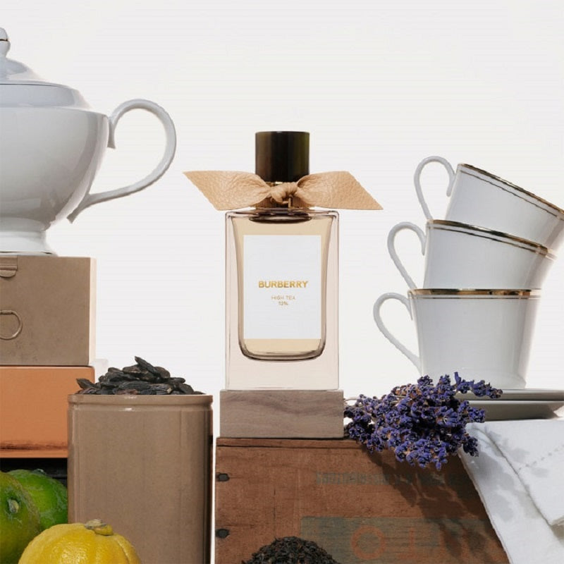 Perfume bottle with a bow on a wooden surface surrounded by tea cups and lavender.