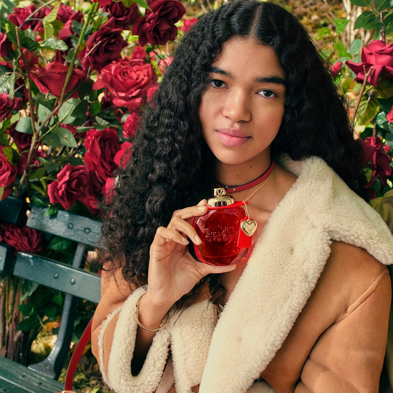 Woman holding a red perfume bottle in a garden setting