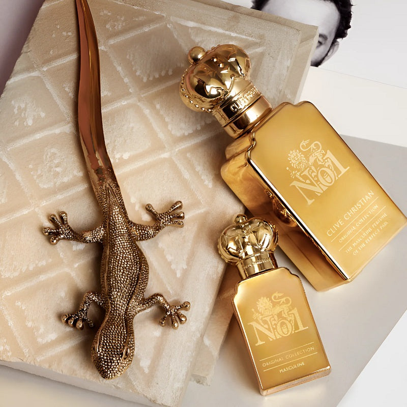 Two gold perfume bottles with a decorative lizard on a textured surface