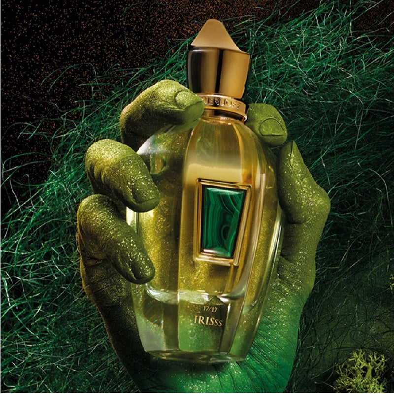 Gold perfume bottle with green accents held by a hand on a green textured background