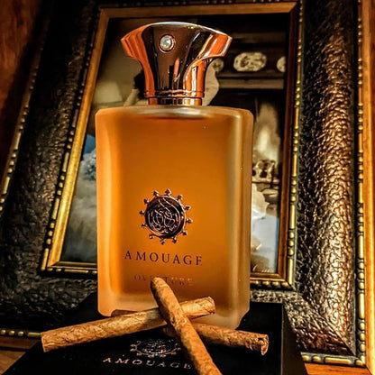 Amouage perfume bottle with cinnamon sticks on a dark surface in front of a decorative mirror.