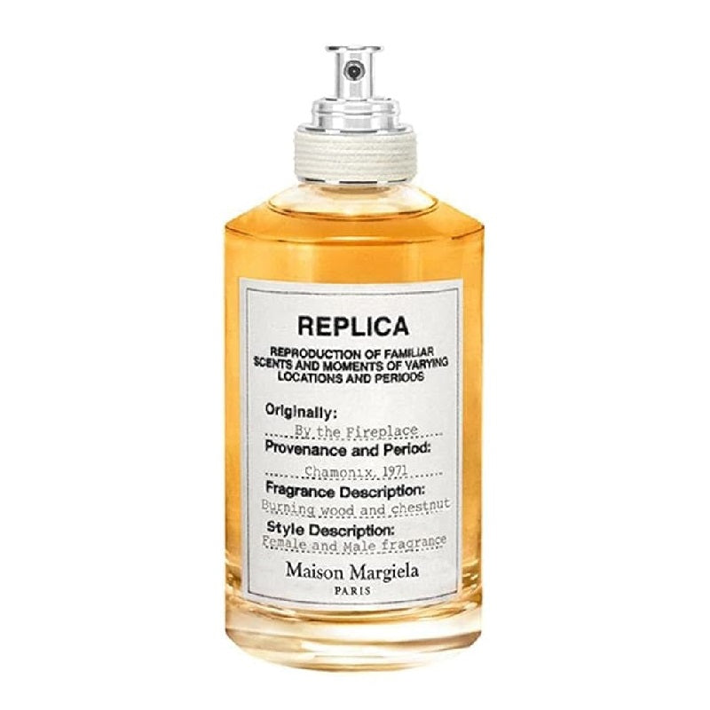A bottle of 'By the Fireplace' Eau de Toilette by Maison Margiela, with a clear, amber-colored liquid visible and a label that includes the product name and a brief description.