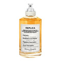A bottle of 'By the Fireplace' Eau de Toilette by Maison Margiela, with a clear, amber-colored liquid visible and a label that includes the product name and a brief description.
