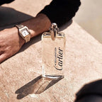 Cartier perfume bottle on a stone surface with a hand wearing a watch in the background