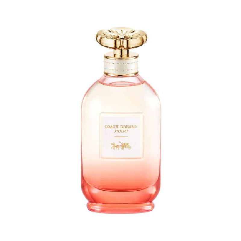 A bottle of Coach Dreams Sunset Eau de Parfum with a pink gradient and a gold-colored cap.
