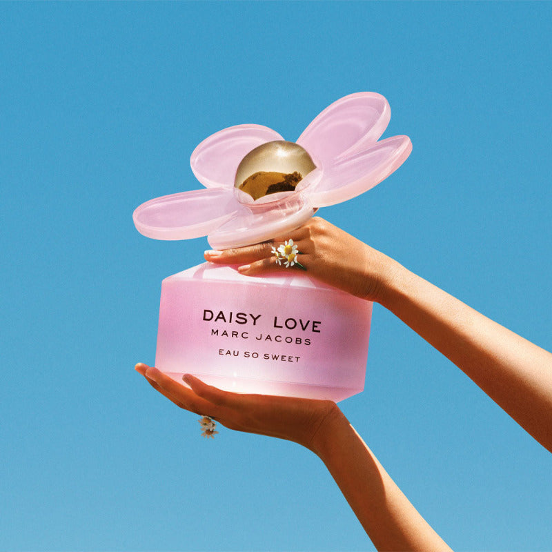 Daisy Love Eau So Sweet Hands holding a pink bottle with a sky blue background