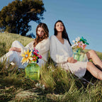Two women sitting in a grassy field with floral perfume bottles.