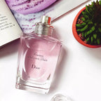 Dior perfume bottle on a white surface with a magazine and plant in the background