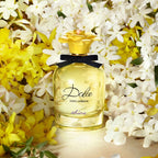 Dolce & Gabbana perfume bottle with yellow cap and black bow, surrounded by yellow and white flowers.