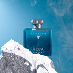 Blue ROJA ELYSIUM perfume bottle on a rocky surface with a blue background