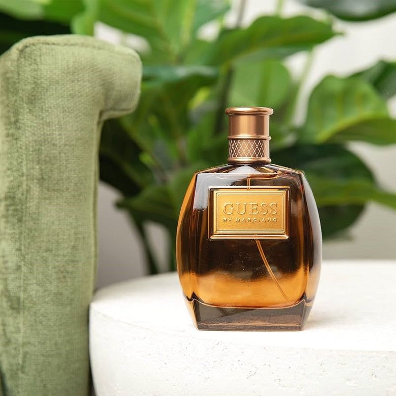 Guess perfume bottle with gold label on a white surface with green plant in the background