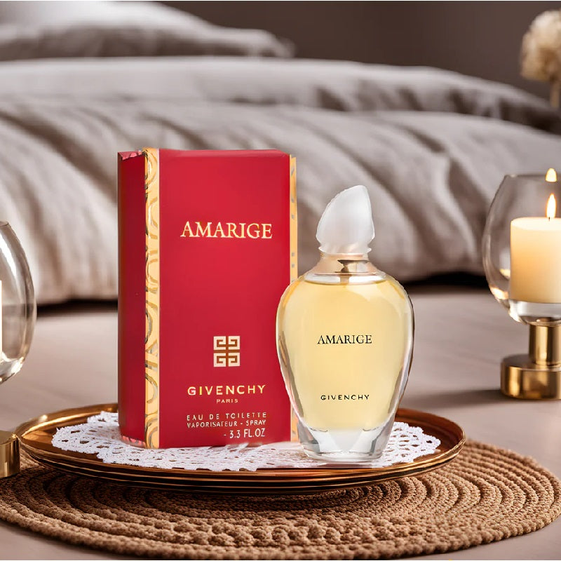 Givenchy Amarige perfume bottle and packaging on a decorative surface with a candle and glassware in the background.