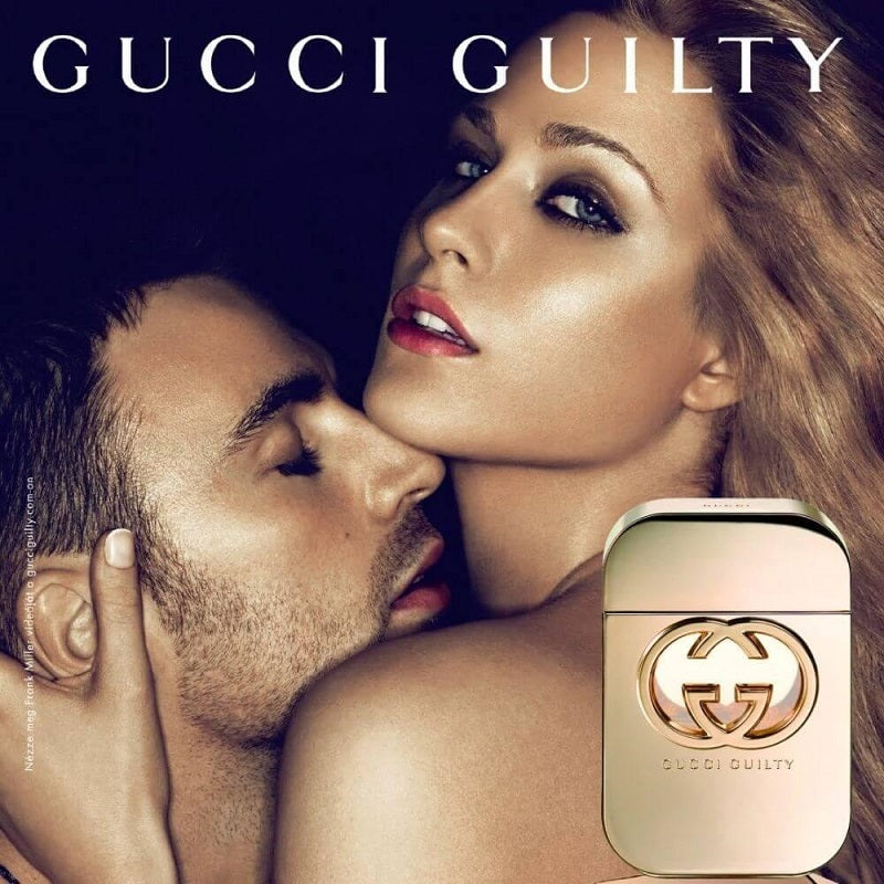 An advertisement image of Gucci Guilty Pour Femme eau de toilette with a gold-colored bottle. A woman is shown with her head tilted upwards, and a man is kissing her on the cheek.