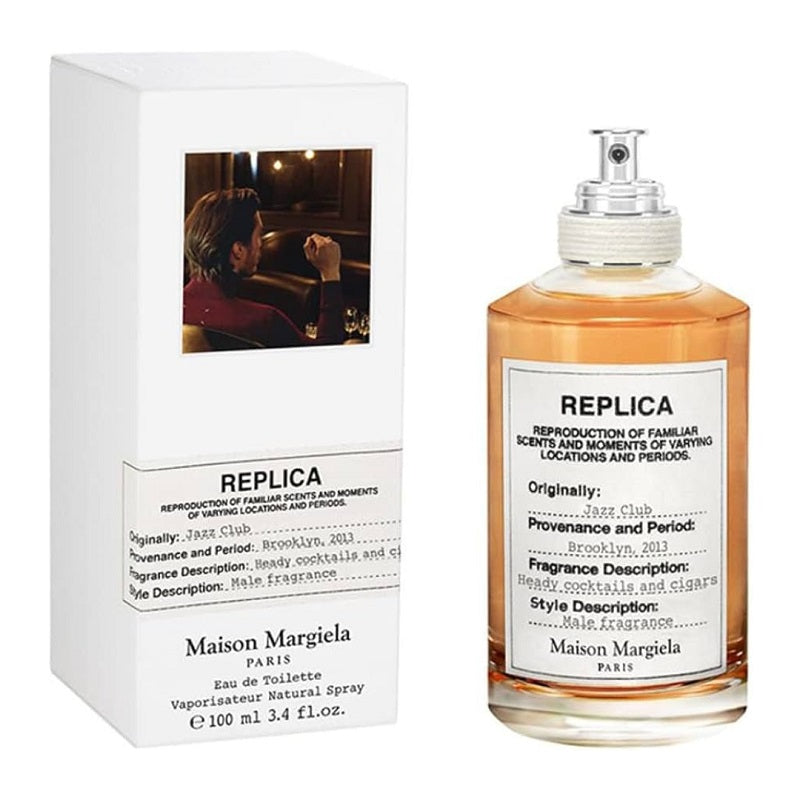 Image showing a 100ml bottle of 'Jazz Club' Eau De Toilette by Maison Margiela, with its packaging box. The bottle is transparent with a golden liquid, and the packaging has a black and white image of a man.