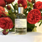 Perfume bottle labeled 'ROSE 31' surrounded by red roses on a white surface.