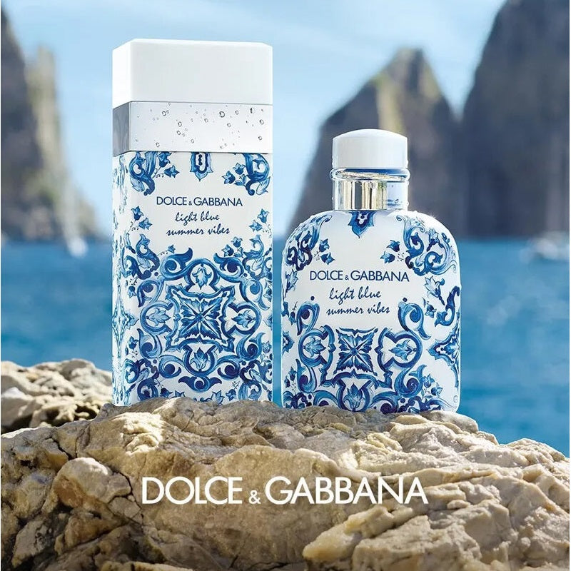 Two Dolce & Gabbana Light Blue Summer Vibes perfume bottles on rocks with a scenic background.