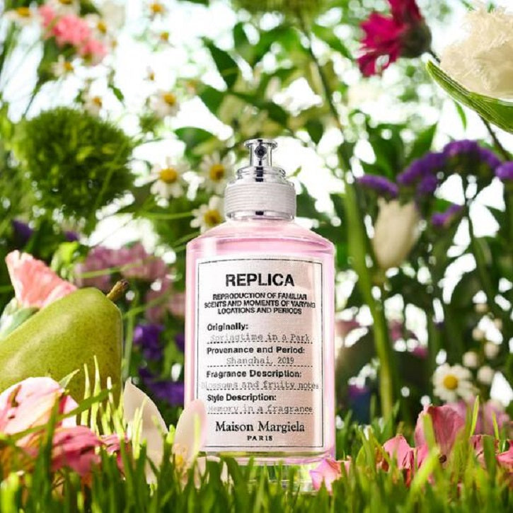 Pink spray bottle labeled 'REPLICA' surrounded by flowers and greenery