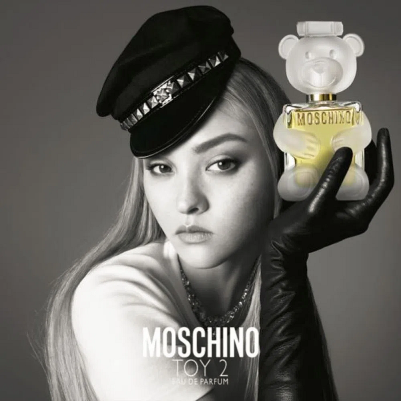 Model holding a Moschino Toy 2 perfume bottle against a gray background