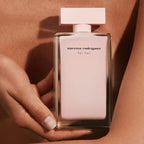 Pink perfume bottle held in a hand against a pink background