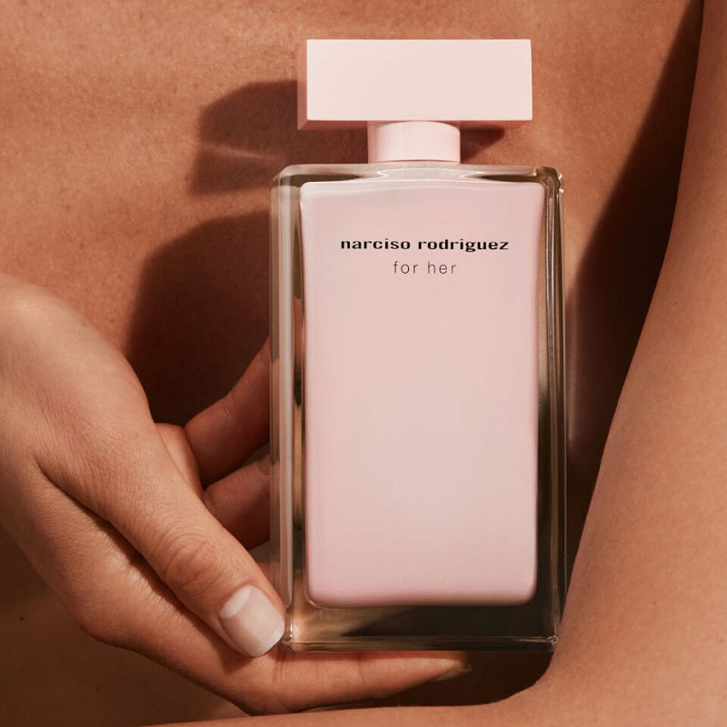 Pink perfume bottle held in a hand against a pink background