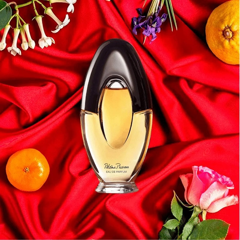 Perfume bottle on a red fabric background with flowers and fruits