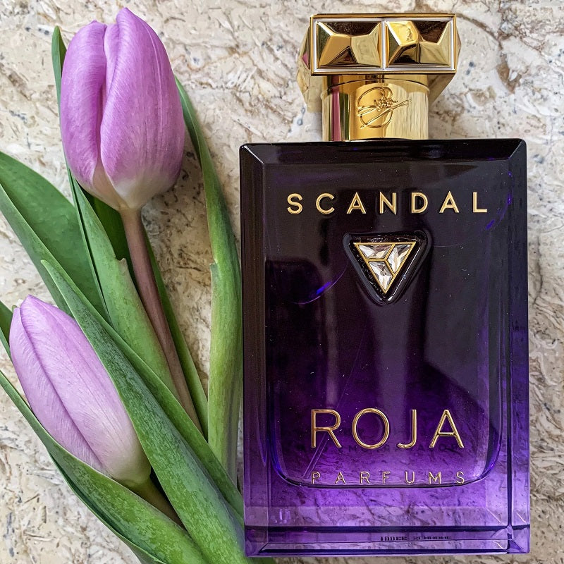 Scandal Roja Parfums perfume bottle with purple tulips on a textured surface