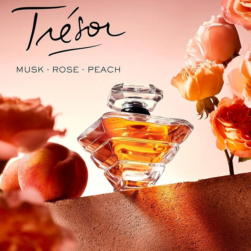 Perfume bottle with flowers and peaches on a soft pink background, featuring the brand 'Tresor'.