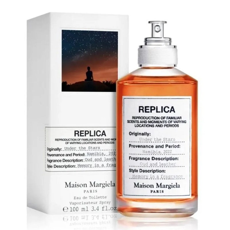 A bottle and package of Maison Margiela Replica fragrance, specifically the 'Under the Stars' variant, with a spray nozzle, labeled with the product name and brand.