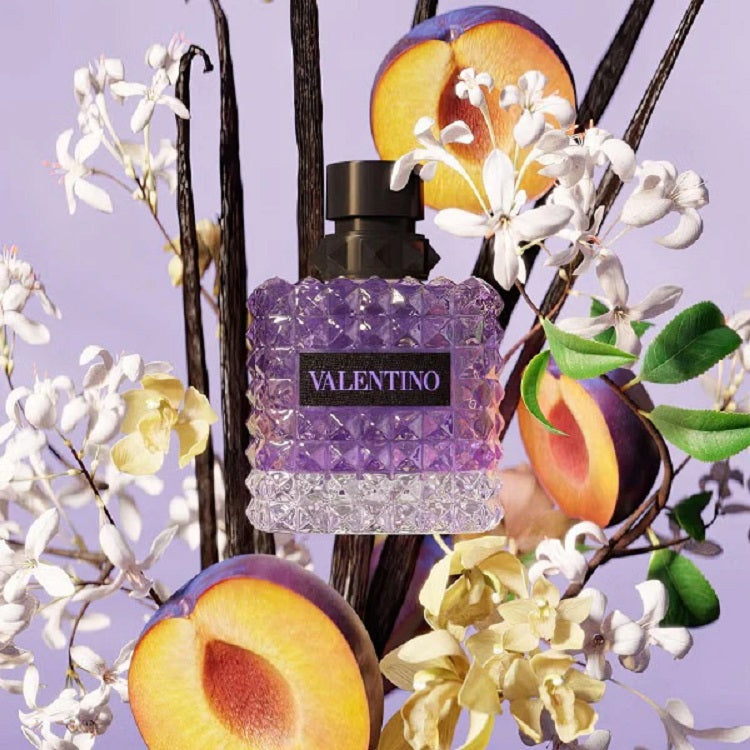 Valentino perfume bottle with peaches and flowers on a purple background