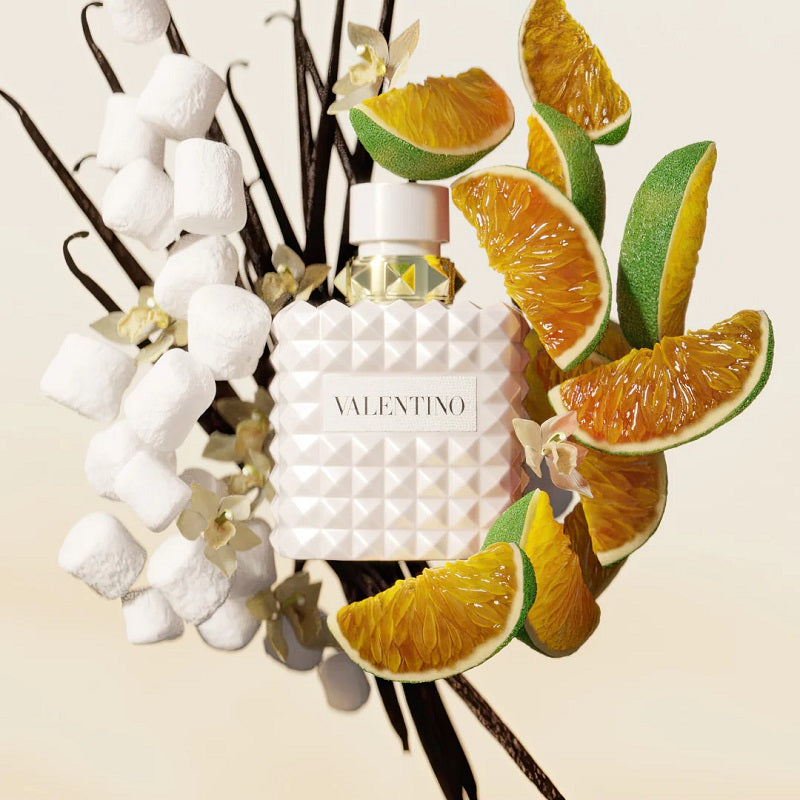 Valentino perfume bottle with vanilla beans, marshmallows, and citrus fruits on a beige background