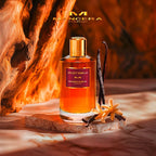Mancera Xpliict Vanilla perfume bottle with vanilla beans and flowers on a wooden platform.