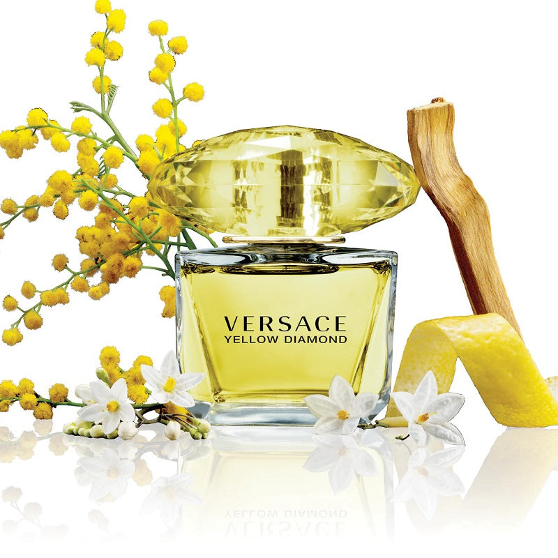 Versace Yellow Diamond perfume bottle with yellow flowers and a lemon on a white background