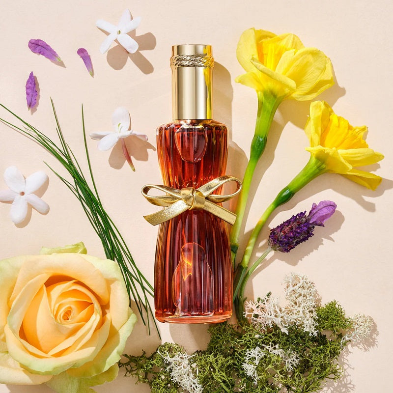 Perfume bottle with a gold bow surrounded by flowers on a beige background