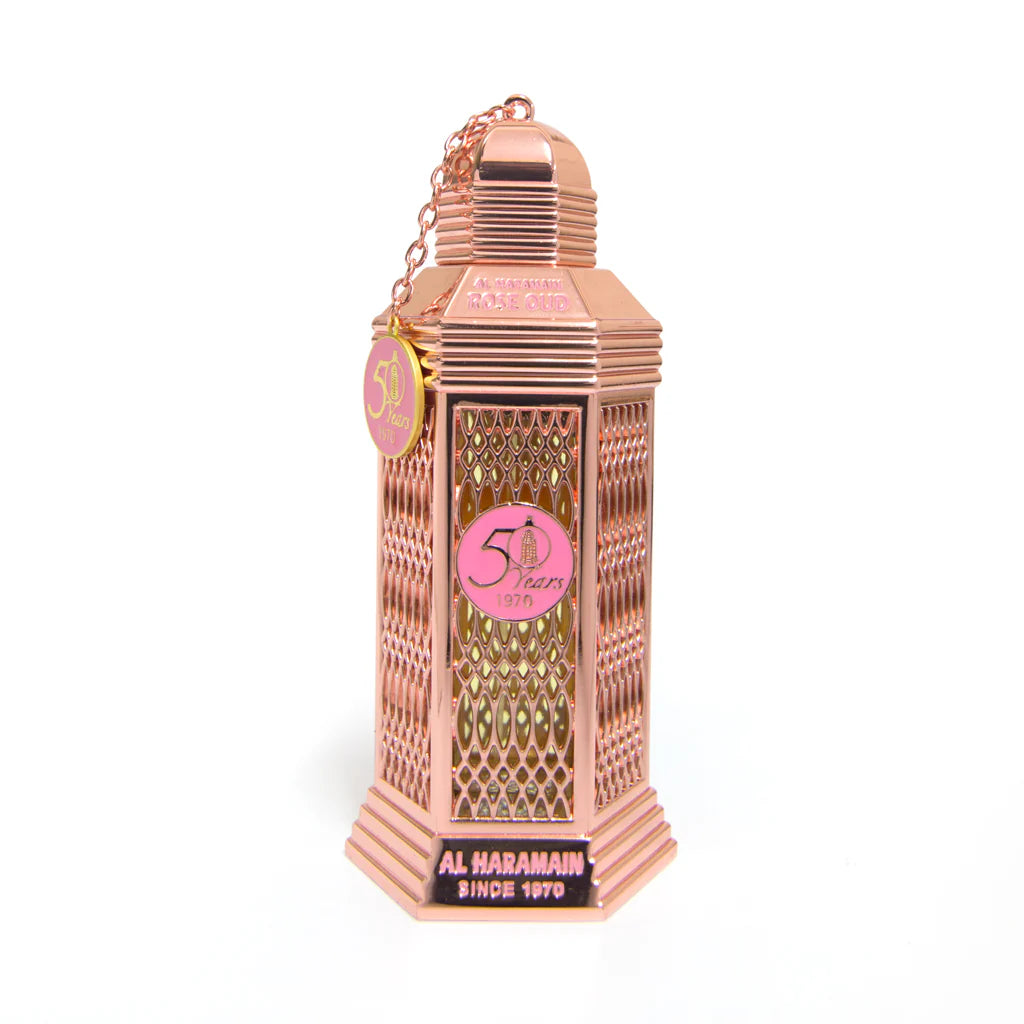 A pink colored bottle of Rose Oud Eau de Parfum by Al Haramain with a decorative cap and label, displayed against a white background.