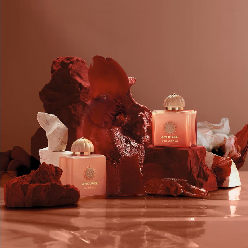 Two pink perfume bottles with gold caps on a textured surface with decorative rocks and crystals.