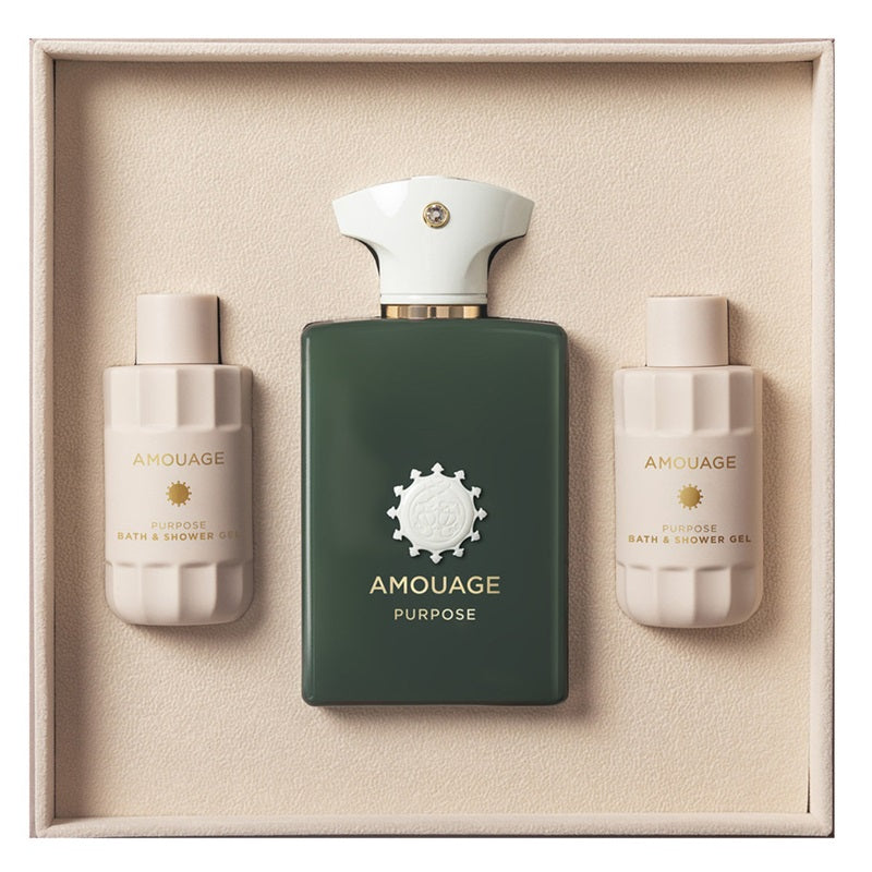 Amouage Purpose bath and shower gift set in a beige presentation box, featuring a dark green rectangular bottle in the center with a white cap, flanked by two cream-colored bottles labeled bath & shower oil and bath & shower gel.