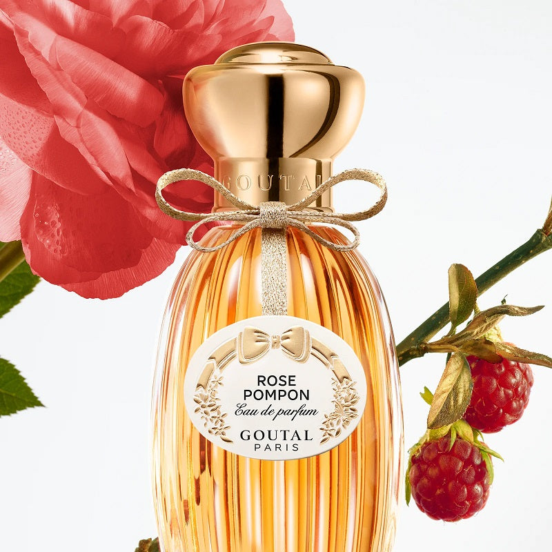 Perfume bottle with gold cap and 'Rose Pompon' label, surrounded by a red rose and raspberries.