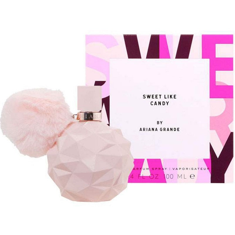 Ariana Grande's 'Sweet Like Candy' perfume, with a pink, faceted bottle and a decorative pom-pom, alongside its purple and pink packaging.