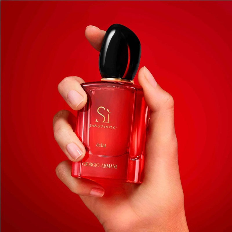 Red Giorgio Armani perfume bottle held in a hand against a red background
