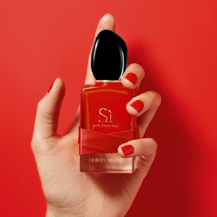 Hand holding a red Giorgio Armani perfume bottle against a red background