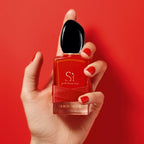 Hand holding a red Giorgio Armani perfume bottle against a red background