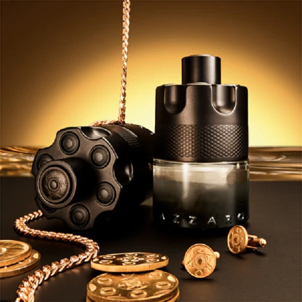 Black perfume bottle with gold coins and chain on a reflective surface