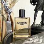 Burberry Hero perfume bottle on a reflective surface with decorative items in the background