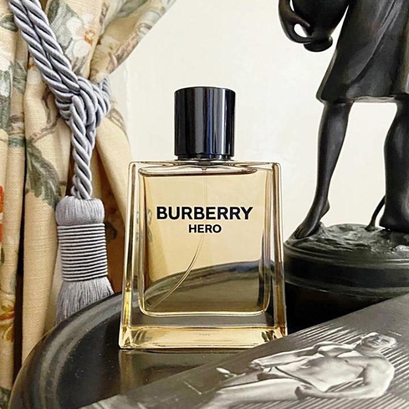 Burberry Hero perfume bottle on a reflective surface with decorative items in the background