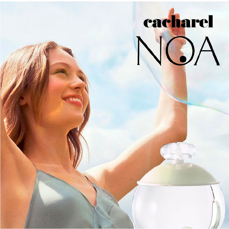 Woman holding a Cacharel Noa perfume bottle against a bright sky.