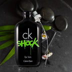 Calvin Klein CK One Shock perfume bottle on a dark background with stones and leaves.