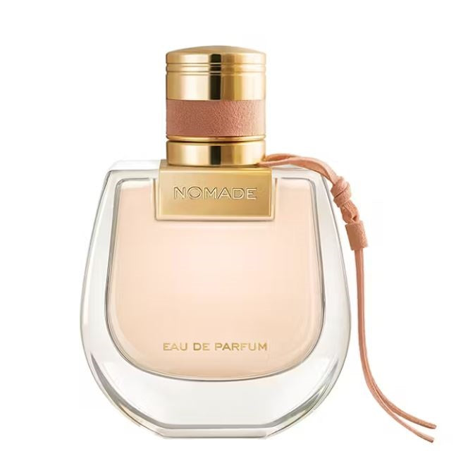 A bottle of Nomade Eau de Parfum by Chloe with a clear glass container, a gold cap, and a pink tie around the neck.