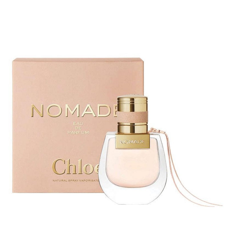 A bottle of Nomade Eau de Parfum by Chloe with its pink box in the background. The bottle is clear with a gold cap and a pink label.