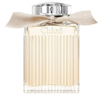 A bottle of Chloe Signature Eau de Parfum with a clear, ribbed design and a beige ribbon at the neck.