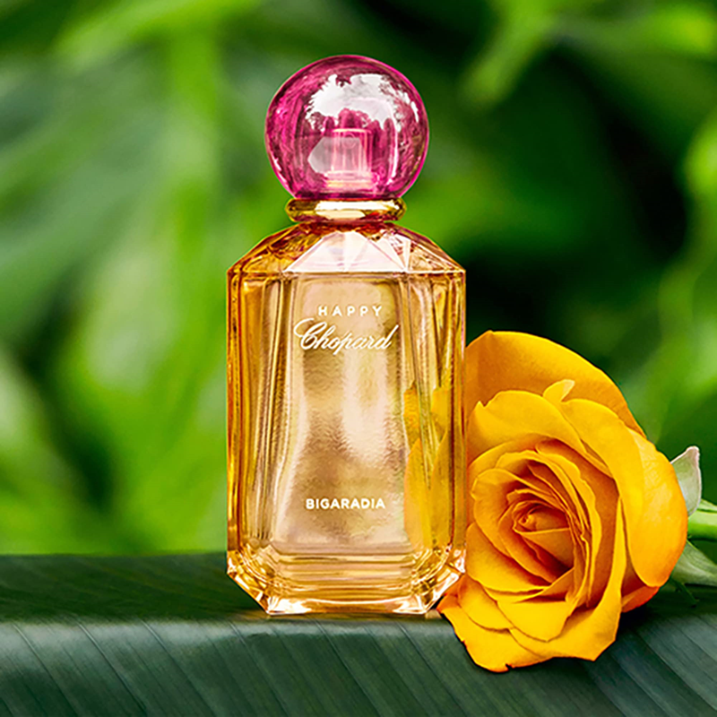 Perfume bottle with pink cap and yellow rose on a green leaf